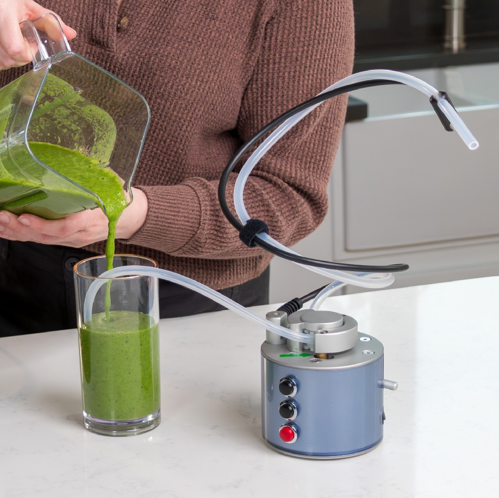Powered drinker pump with tubing, an example of adaptive equipment for Parkinson's, beside a glass of green smoothie